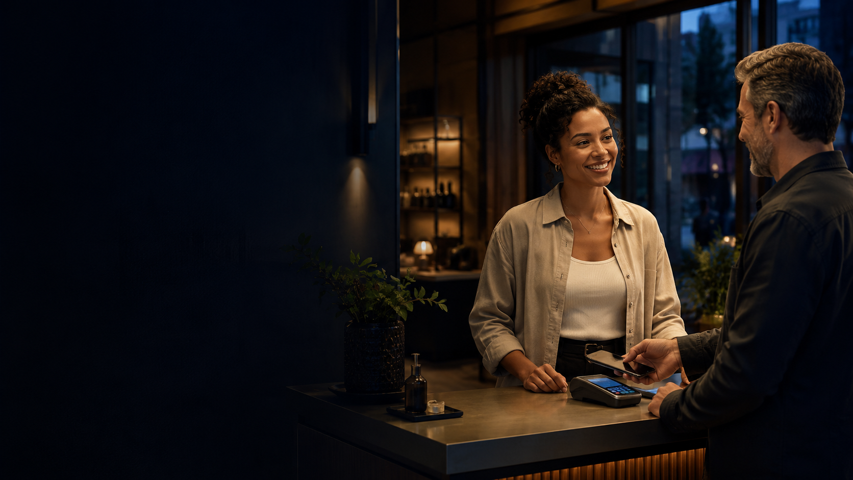 A business owner at a premium branded checkout, mid-interaction with a returning customer at dusk